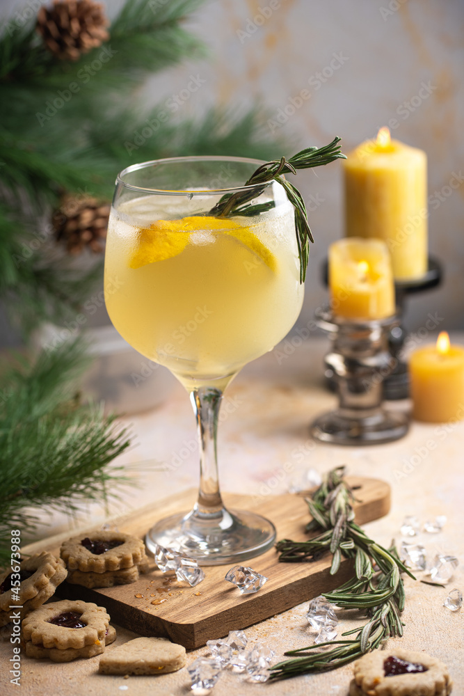 A big glass with christmas drink lemonade with rosemary and lemons surrounded by christmas decoration, lights and candles