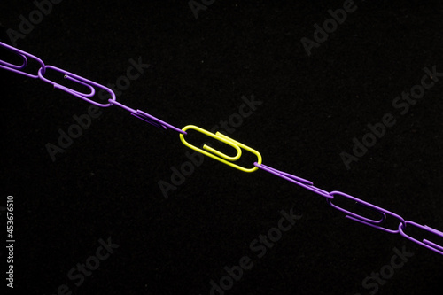 Linked paper clips on a dark background. One link of a paper clip differs in color
