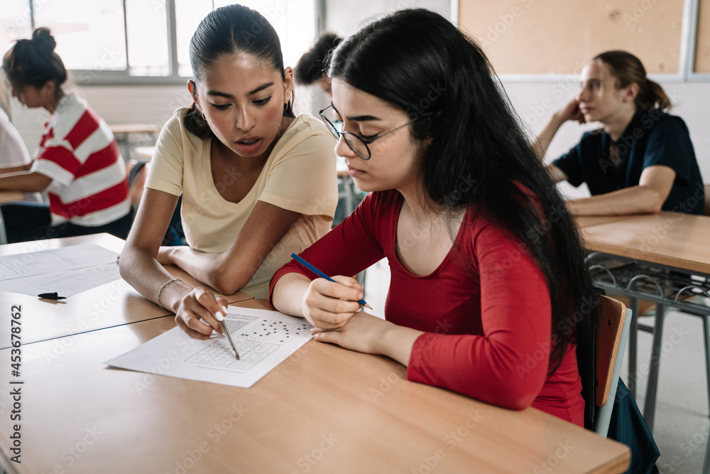 Two latin and hispanic female classmates friends together in the High School Classroom during an exam Two latin and hispanic female classmates friends together in the High School Classroom during an exam