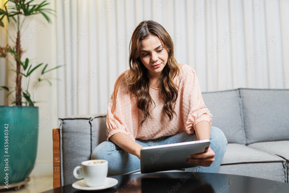 Happy Latin lady relax drinking coffee at home alone sit on room using digital tablet. Happy Latin lady relax drinking coffee at home alone sit on room using digital tablet.