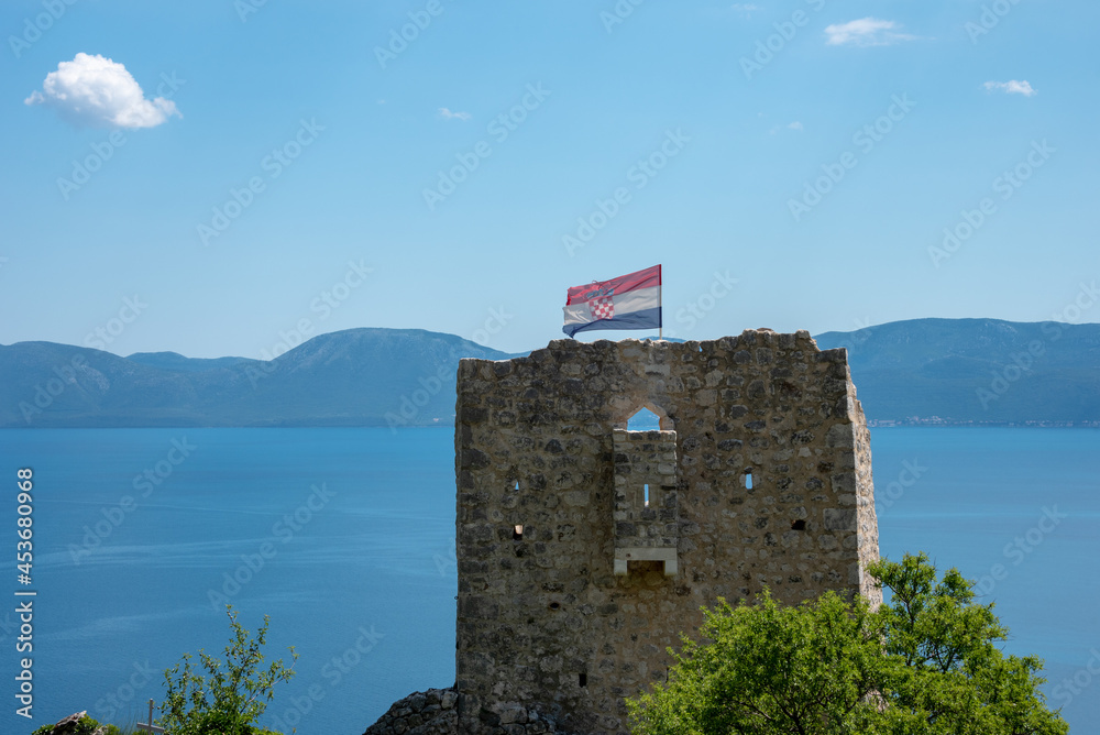 Ruins of the tower on the top of the hill. Flag on the wind. Podaca Village, Makarska Riviera, Dalmatia Croatia. Shore of Adriatic Sea. 