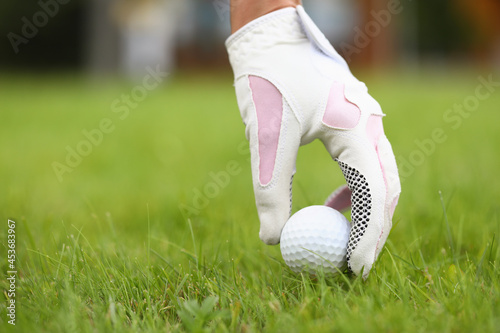A hand in a glove puts a golf ball on the grass