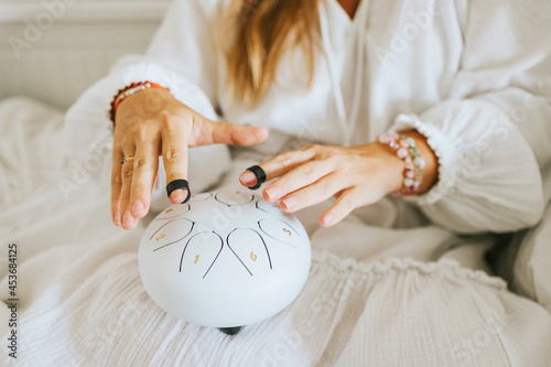 white drum glucophone and drum sticks on the lap of a young woman plus size model in white dress meditates while playing on instrument,  drum for meditation and mental health photo