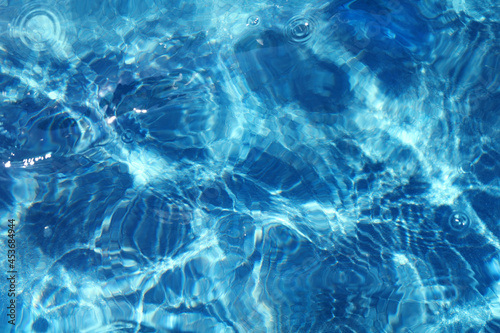 Azure rippled water surface of blue swimming pool. Background of water ripple under bright sunny sky with few drops. Full frame texture. Summer holidays, vacations resort concept.