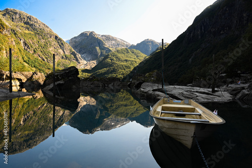 The mountain scenery and a boat reflect in the water of the Norwegian glacier lake Bondhusvatnet. photo