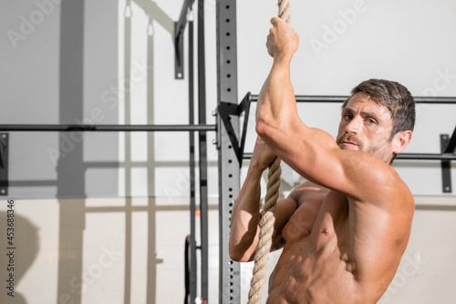 Fitness man doing rope climb exercise in gym. High quality photo.