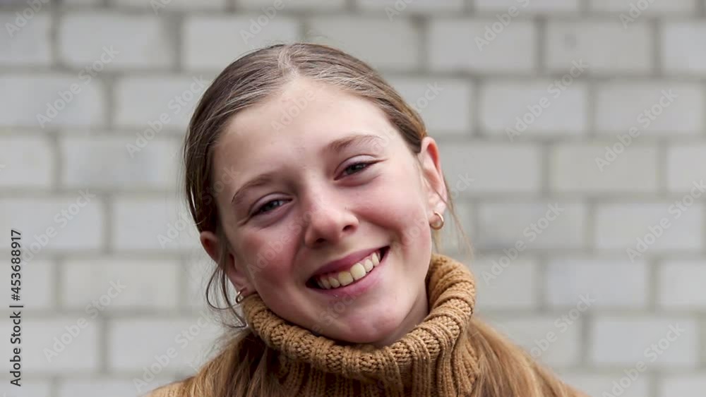 Defocus outdoor portrait of a cute little 10 year old girl on white brick background. Cute girl in knitted sweater portrait outside. Little child often blinks and looking at camera. Out of focus