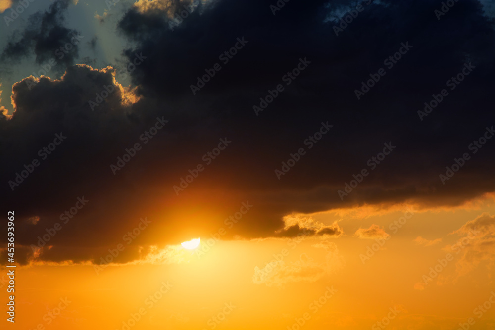 The sun is going down among the clouds. Close up view to the sunset and picturesque clouds of bright orange and yellow colors.