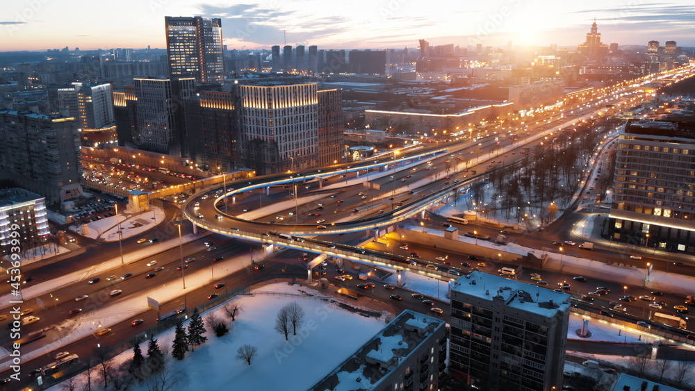 View from above to Moscow multi-level highway in winter lit by the sunset light. Camera showing panorama of the evining city and then coming closer to the junction with a lot of traffic.