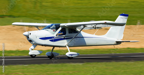 View of sports airplane in motion over runway on background with picturesque landscape.