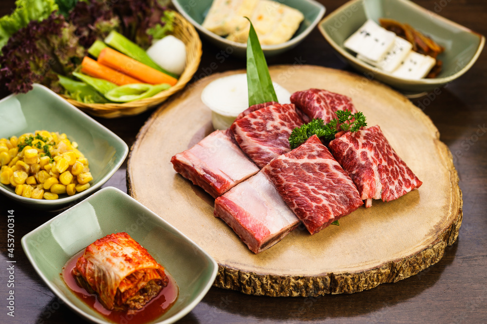 Fresh and raw expensive A5 Wagyu marble beef meat ready to grill on a wooden tray with kimchi side dish and vegetable. Traditional Korean BBQ or Japanese Yakiniku Barbecue concept. Selective focus. Fresh and raw expensive A5 Wagyu marble beef meat ready to grill on a wooden tray with kimchi side dish and vegetable. Traditional Korean BBQ or Japanese Yakiniku Barbecue concept. Selective focus.