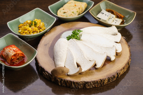 Fresh, raw sliced Eringi or King Oyster Mushroom on wooden tray with kimchi side dish and vegetable. Vegetarian, vegan and meatless. Korean BBQ or Japanese Yakiniku Barbecue concept. Selective focus. photo