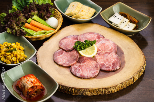Fresh and raw expensive A5 Wagyu beef tongue meat ready to grill on a wooden tray with kimchi side dish and vegetable. Traditional Korean BBQ or Japanese Yakiniku Barbecue concept. Selective focus.