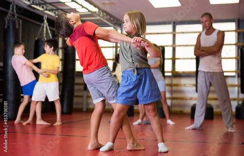 Girls and boys performing self-defence moves in gym during their group training.