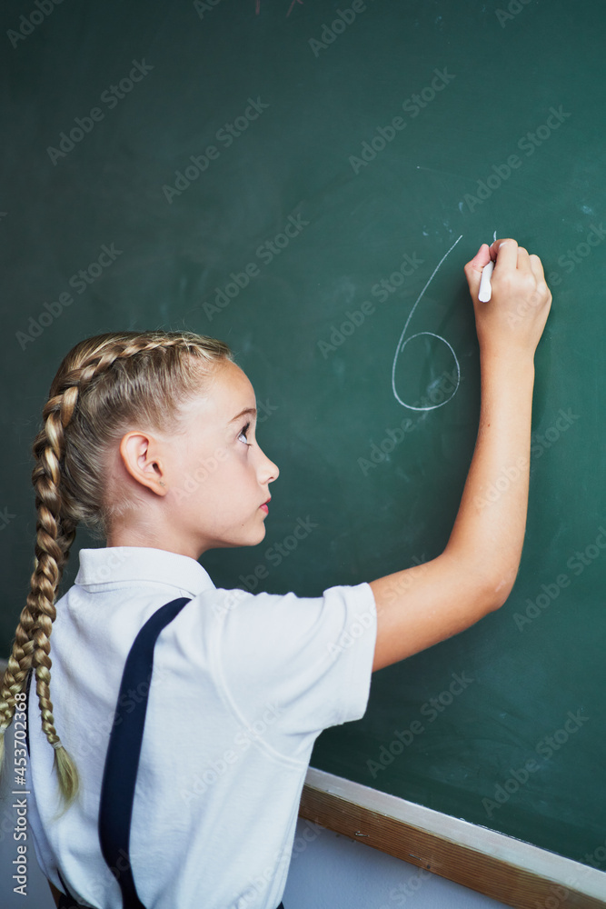 Portrait of young girl writing numbers on chalkboard at school