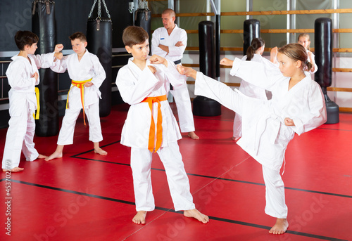 Preteen children practicing in pair karate movements with male trainer supervision