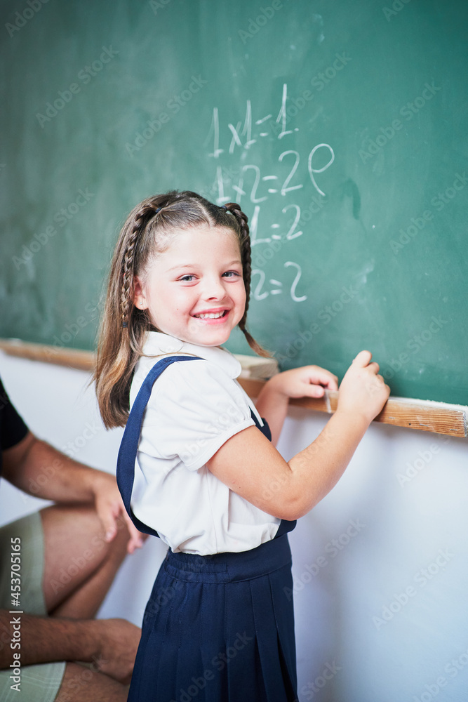 Young brunette school girl standing next to chalkboard looking at camera