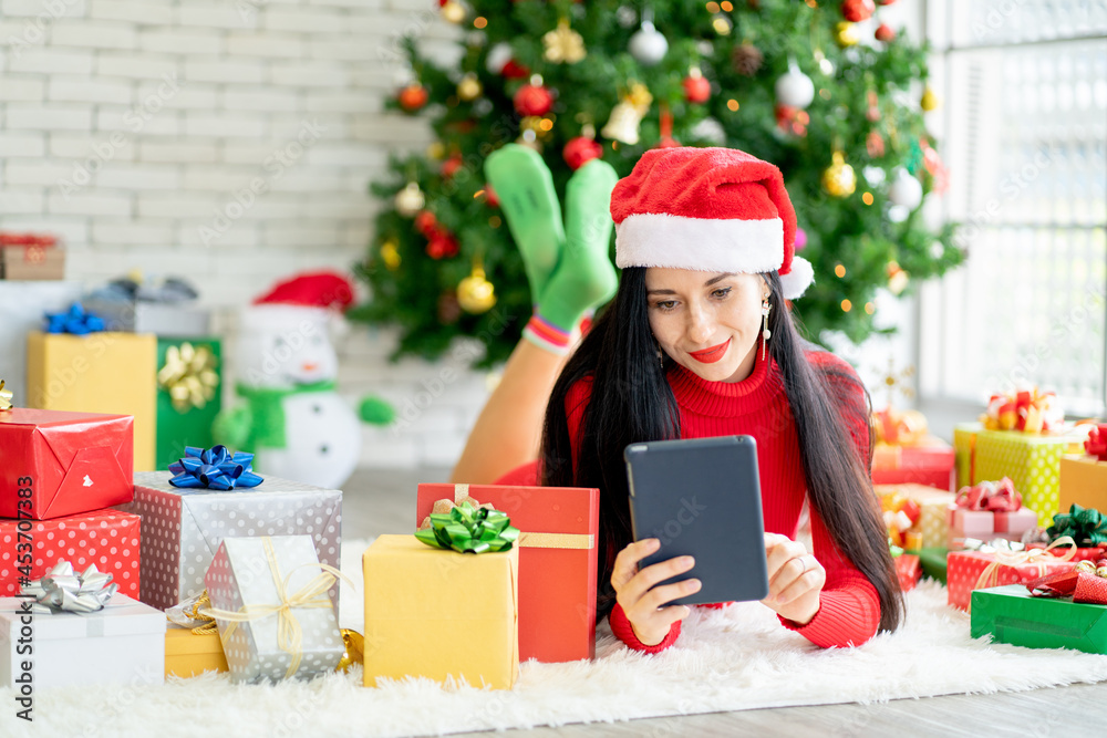 Pretty woman lie on floor among decoration of Christmas festival and she use tablet look like for online shopping with happiness.