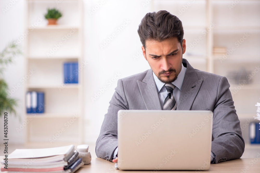 Young male employee unhappy with excessive work in the office Young male employee unhappy with excessive work in the office
