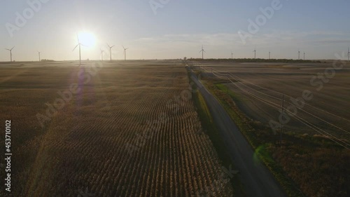 Aerial flying over a road in North Dakota farmland towards windmills in the evening with the sun setting and distant windmills spinning photo