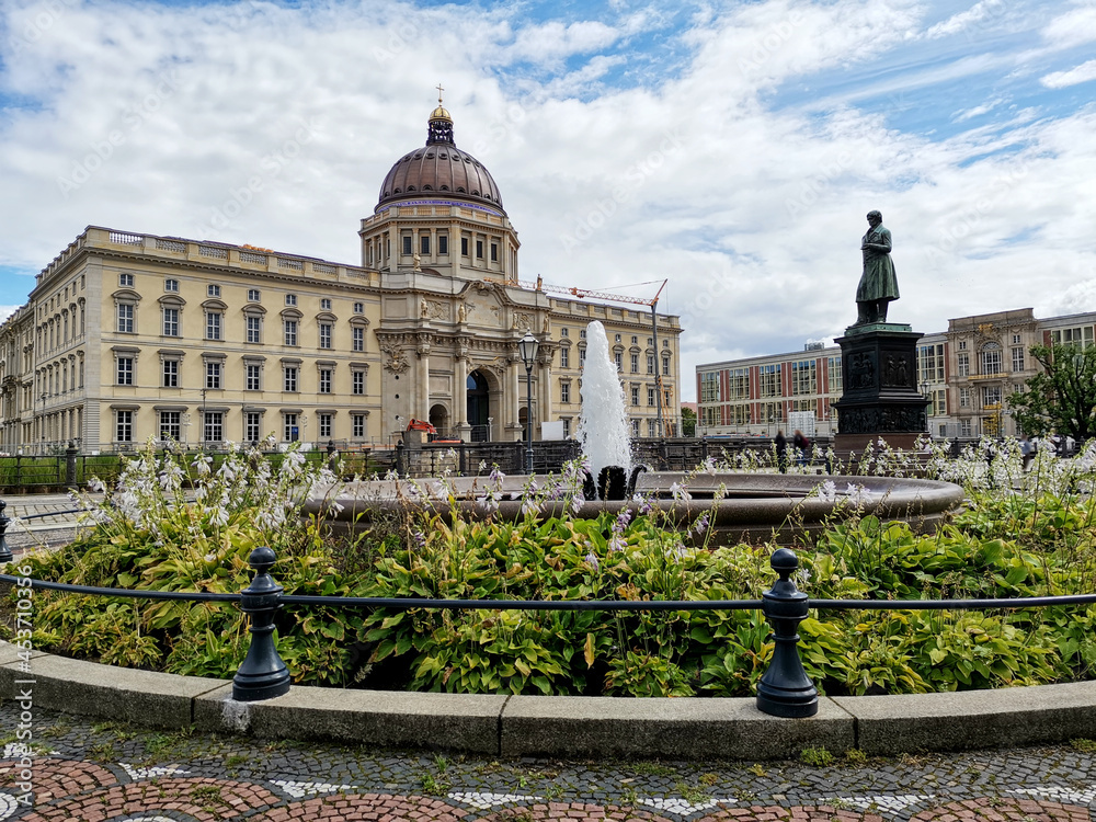 Fototapeta premium Humboldt Forum museum building facade with splashing fountain and statue under blue cloudy sky in Berlin, Germany