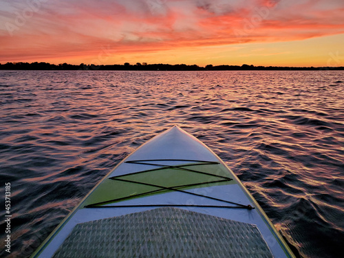 Paddleboard floating on the water with the colorful light of sunset reflecting off the waves of a lake at dusk