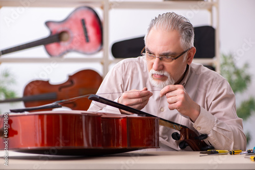 Obraz na plátně Old male repairman repairing musical instruments at workplace