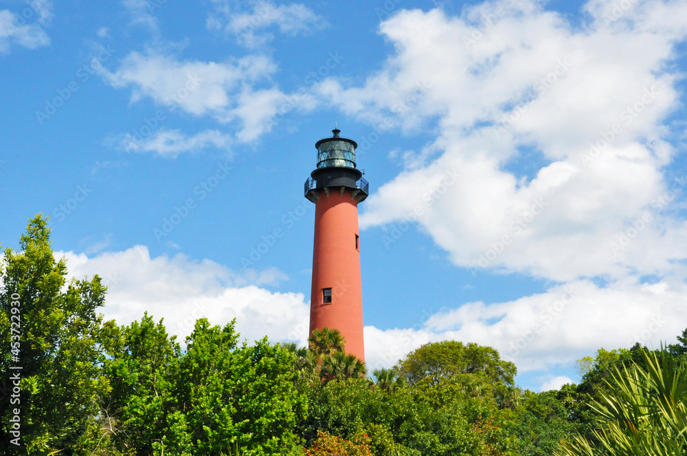 Medium shot view of a vibrant coral orange lighthouse in the center of the photo with clouds and trees Medium shot view of a vibrant coral orange lighthouse in the center of the photo with clouds and trees