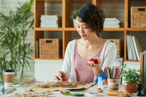 Young woman practicing oshibana art, she is using pressed flowers and other botanical materials to create entire picture