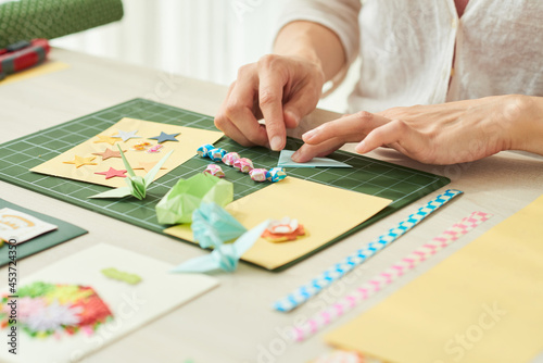 Close-up image of woman making elements like stars, crane or flowers for greeting cards out of colored paper