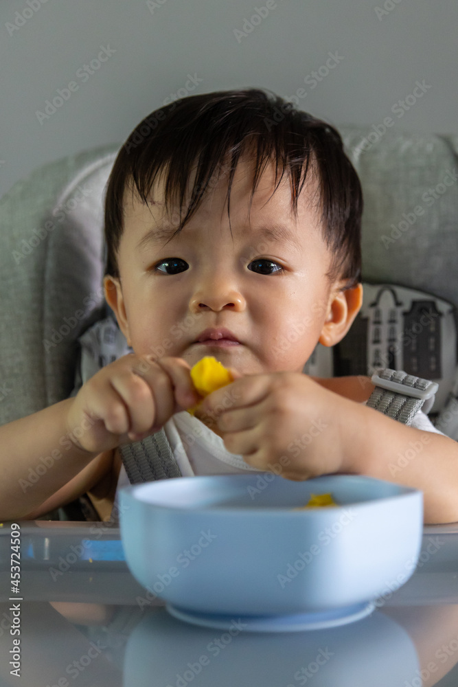 adorable and cute happy Asian Chinese baby boy siting on baby chair enjoying his lunch adorable and cute happy Asian Chinese baby boy siting on baby chair enjoying his lunch