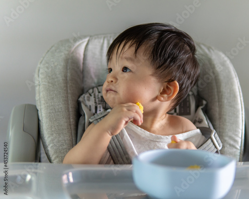 adorable and cute happy Asian Chinese baby boy siting on baby chair enjoying his lunch