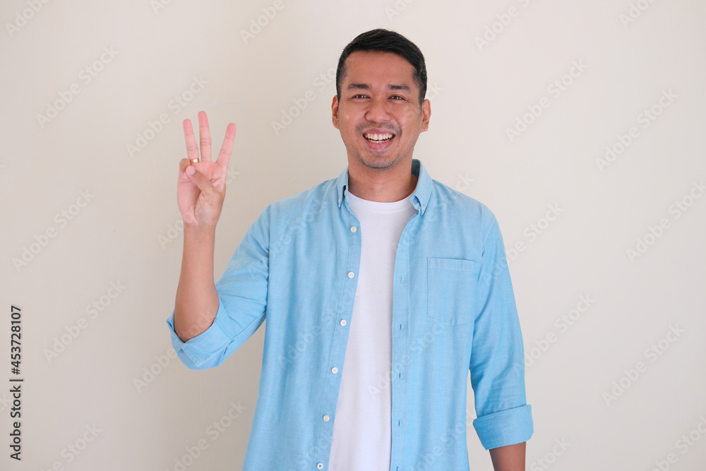 Asian man smiling happy while giving three finger up symbol Asian man smiling happy while giving three finger up symbol