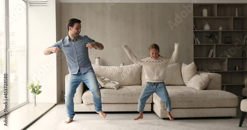 Young cheerful man have fun enjoy active dances with cute little daughter in cozy living room, full-length view. Carefree leisure time together at home, family weekend funny activities, hobby concept