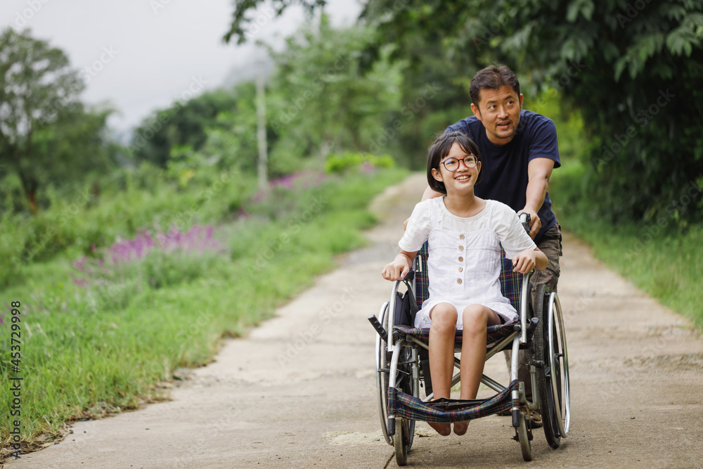 Father and Disabled child on wheelchair walking on trail park in sunny day. Happy disability kid travel in family holiday concept. Father and Disabled child on wheelchair walking on trail park in sunny day. Happy disability kid travel in family holiday concept.