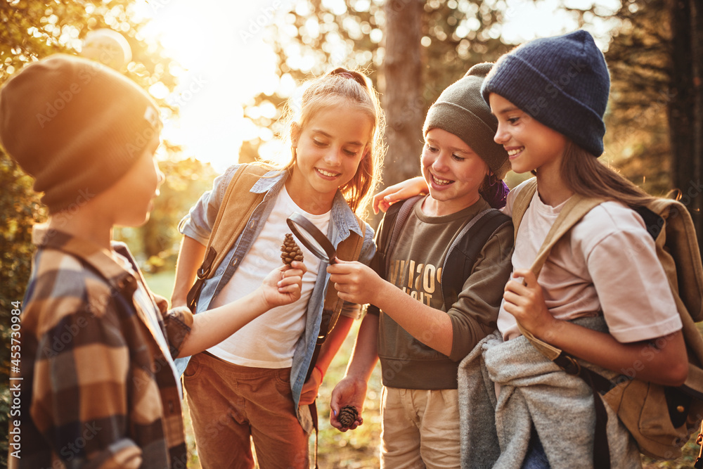 Obraz premium Group of happy school kids in casual clothes with backpacks exploring nature and forest together