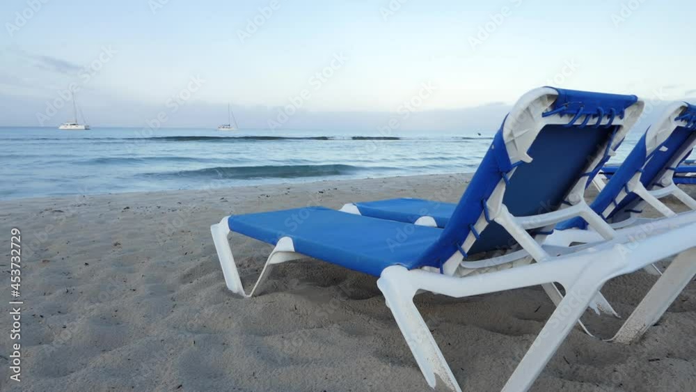 View from the back of sunbeds in an empty beach, small waves on the sea, dream luxury travel inspiration. Boats and sailboats at mooring. View from the back of sunbeds in an empty beach, small waves on the sea, dream luxury travel inspiration. Boats and sailboats at mooring.