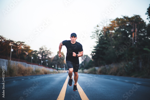 Athletic man runner work out on street. Sportive Asian Male running in the middle of the road and looking at camera. Healthy lifestyle photo