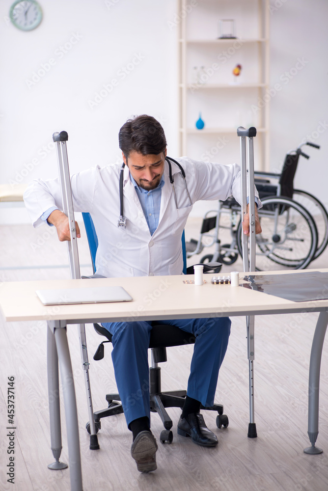 Young male doctor with crutches working in the clinic Young male doctor with crutches working in the clinic