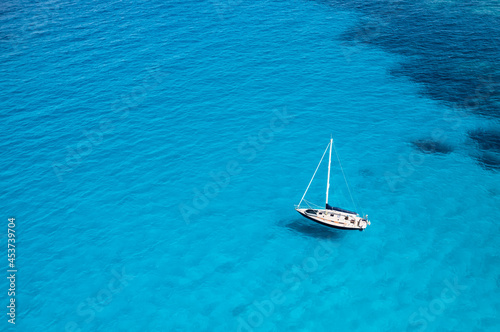 View from above, stunning aerial view of a sailboat floating on a turquoise, crystal clear water during a sunny day. Costa Smeralda, Sardinia, Italy. © Travel Wild