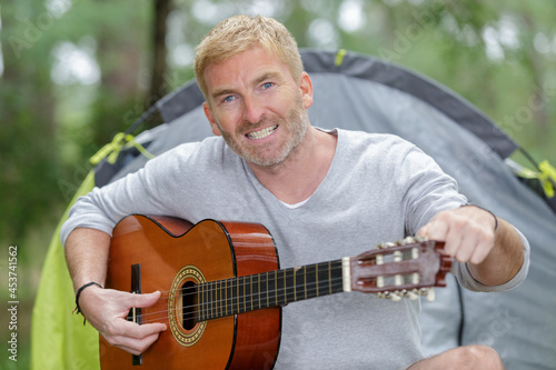 mature man playing guitar on campsite