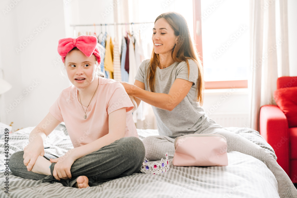 Obraz premium Woman doing hairstyle for her daughter with down syndrome