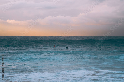 silhouette of surfers at sunset in the ocean waiting for a wave to catch © Em Neems Photography