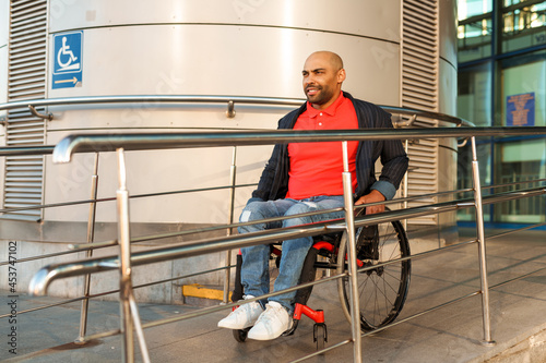 Man wearing jacket riding in wheelchair on ramp by building photo