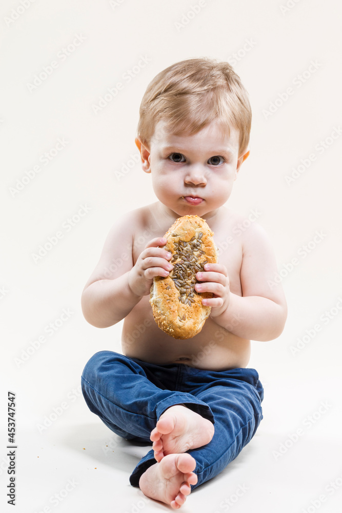 Closeup Portrait of Little Child With Food in Hands While Eating Freshly Baked Bun And Posing Against Beige Background