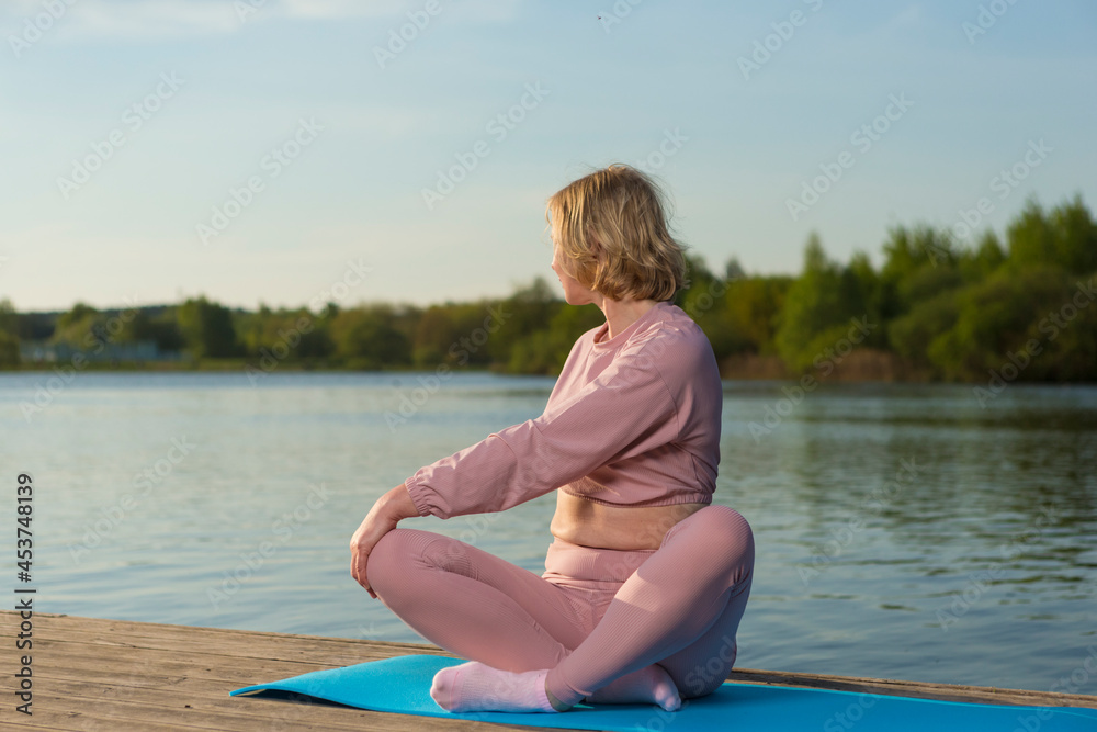 Sport Ideas. Senior Caucasian Woman in Sport Outfit Practicing Stretching Yoga On Wooden Stage Near Water Outdoor.