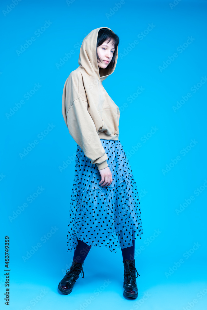 Naklejka premium Young Dancing Brunette Girl in Street Clothing Posing In Headphones and Hoodie in Dance Pose Over Blue Background.