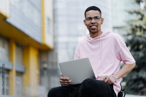 Handsome young man in glasses working on laptop outdoors on a background of corporate building