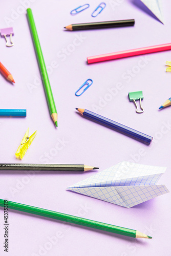 Paper airplane with pencils and clips on color background