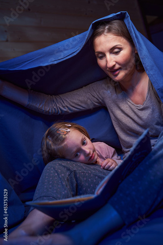 Parent with kid with book covering themselves with blanket
